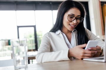 Poster - selective focus of happy businesswoman using smartphone near laptop