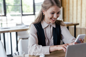 selective focus of beautiful businesswoman smiling while using smartphone in office