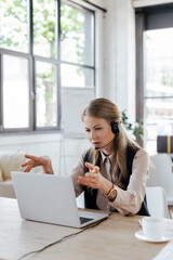 Poster - selective focus of attractive operator in headset gesturing while talking near laptop and cup