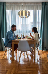 Wall Mural - Young couple eating salad while sitting at a table at home.