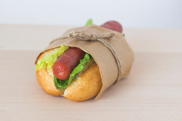 One classic homemade hot dog with fresh green salad in eco-packaging on a light wooden background.American Fast Food.National hot dog day holiday.