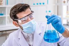 Arab Male Researcher Scientist Holding And Examine Erlenmeyer Flask Filled With Blue Liquid Chemical In Laboratory