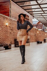 Beautifulmodel posing for photos on the street. Wearing beige skirt, black blouse, black boot and hat.