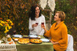 Women sit at the festive autumn table with pies and clink glasses of wine and laugh. Festive family dinner in the backyard.