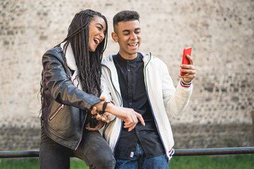 A couple of mixed race best friends having fun together using a smartphone. Young people watching funny videos on the cell phone. boy and girl having positive emotions and technology concepts.