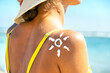 © bilanol - Back view of young woman tanning at the beach with sunscreen cream in sun shape on her shoulder. UV sunburn protection and sunblock skincare concept