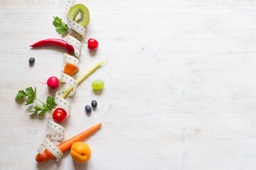 Wall Mural - Vegetables and fruits between measuring tape on white background. Healthy diet concept