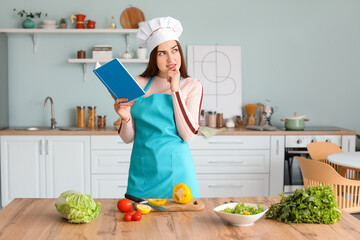 Young woman with recipe book cooking in kitchen