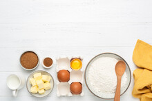 Baking Ingredients On White Wooden Table. Ingredients For Baking Pastry Cake Or Cookies. Bowl Of Wheat Flour, Eggs, Cubed Butter, Sugar Milk And Spices. Top View With Copy Space For Text, Design Or Re