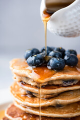 maple syrup pouring on stack of pancakes closeup view. sweet golden maple syrup pouring on blueberry