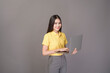© tonefotografia - young confident beautiful woman wearing yellow shirt is holding a laptop on grey background studio