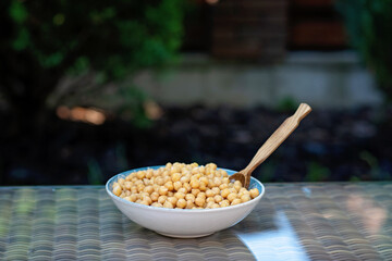 Bowl with boiled chickpeas with a wooden spoon on the table outdoor. Healthy vegetarian food. Copy spase.