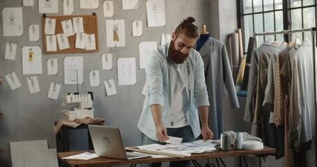 Wall Mural - A hipster clothing designer working in his loft office, creating a new clothes collection, looking at camera and smiling - fashion, small business concept 4k footage