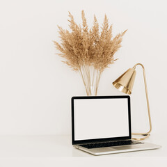 Wall Mural - Laptop with blank copy space screen on white table with golden lamp and pampas grass / reeds bouquet. Minimalist home office workspace. Mockup template.