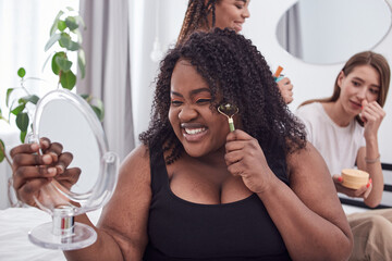 Smiling Afro American woman massaging face with a roller