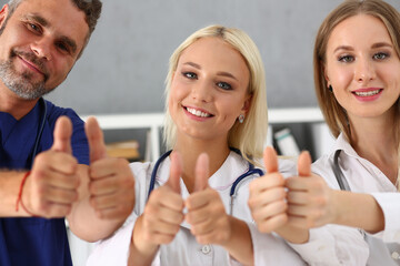 Happy successful young pediatricians looking at camera and standing in the office together with thumbs up. Medicine and health concept