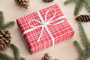 Sticker - Red christmas gifts surrounded with pine cones, leaves and twine on a wooden table.