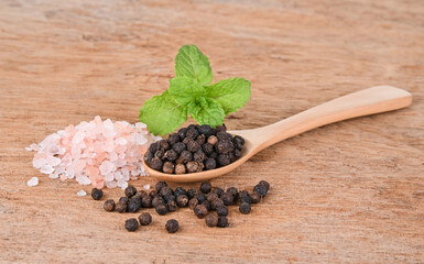 Black pepper in a wooden spoon with pink salt in wooden background