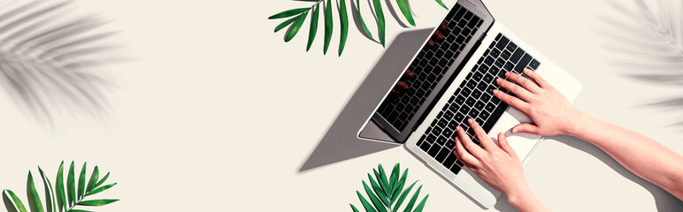 Canvas Print - Person using a laptop computer with tropical leaves from above