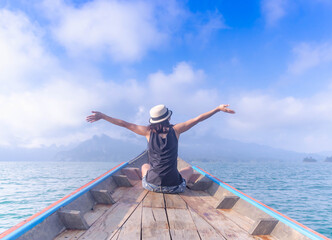 Asian traveler woman sitting and raising her hands  in the air on boat,Freedom concept.