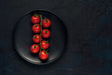 A Truss Of Red Wet Cherry Tomatoes In Black Plate On A Dark Textured Background. Top View. Space For Text.