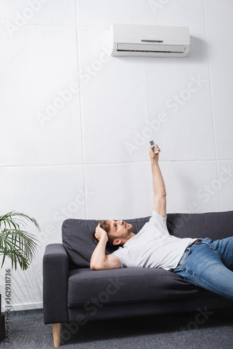 Fotomural confused man holding remote controller and suffering from heat with broken air c