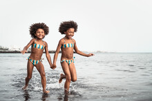 Happy Sisters Running Inside Water During Summer Time - Afro Kids Having Fun Playing On The Beach - Family Love And Travel Vacation Lifestyle Concept