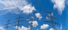 Large Metal High Voltage Lattice Crosses Transporting Electricity Under A Blue Sky With White Clouds