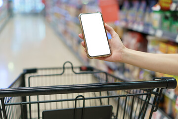 Wall Mural - Mockup, hands holding blank white screen mobile phone with shopping cart in supermarket, digital payment concept