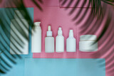Fototapeta  - Simple Blank white Plastic Bottles Set.set of cosmetic products on a pink blue background. Cosmetic package collection for cream, soups, foams, shampoo.Mock up white cosmetic bottles with palm leaf.