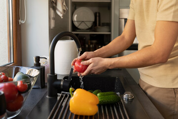 A man washes vegetables in the kitchen sink.