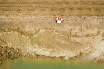 Top view of two road construction workers in orange vests and protective helmets in the middle on the field