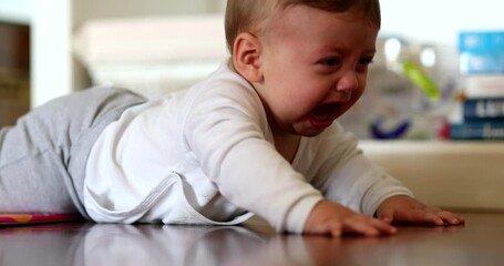 Wall Mural - Baby infant lying on floor starts to cry. Upset angry toddler boy