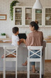 © Olena Bloshchynska - Mother and her son sitting at kitchen and using laptop.