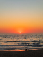 Wall Mural - Vertical Image - Orange sunset lights up the sky and glows golden over the water and sandy beach