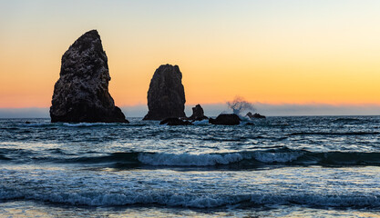 Wall Mural - Waves splashing on Sea Stacks with orange sunset glowing in sky