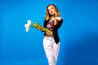Studio portrait of beautiful elegant woman sending air kisses, wearing elegant outfit, holding bouquet of white tulips, blue background, spring vibes.