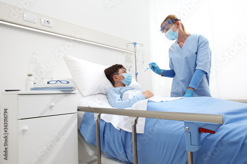 nurse with thermometer measures fever on patient child in hospital bed, wearing protective visor and surgical mask, corona virus covid 19 protection concept,