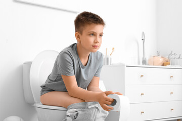 little boy sitting on toilet bowl in restroom