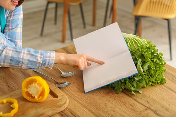 Young woman with recipe book cooking in kitchen