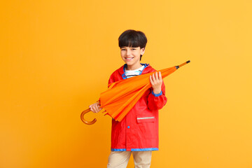 Wall Mural - Cute little boy in raincoat and with umbrella on color background