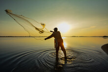 Fisherman Casting Fishing Net In Lake During Sunset