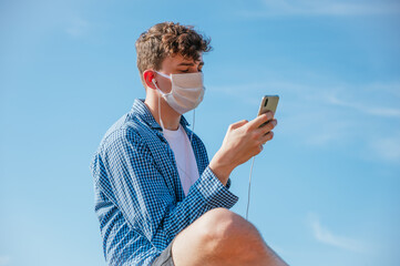 Young man wearing face mask, using smartphone and listening to music