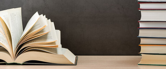 The book is open, the sheets are fan-shaped on a black background next to a stack of books.