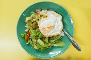 fried garlic cabbage with chili and fried egg eat with rive on green dish over yellow table background