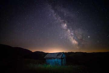 Small abandoned barn farm house shot in the night against a starry sky with milky way galactic core seen above