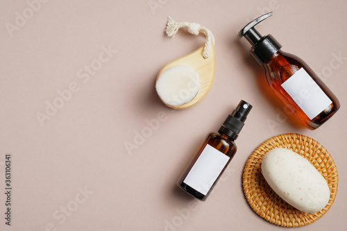 Bathroom cosmetics set on beige background. Flat lay, top view amber glass pump bottle, sprayer, body brush, natural soap. Beauty products packaging mockups with white blank labels.