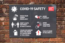 COVID 19 Safety Information Sign For Shoppers Mounted On Brick Wall Leading To Town Centre Shopping Area