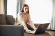 © VERSUSstudio - Young woman with modern laptop sitting on sofa at home