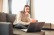 © VERSUSstudio - Young woman with modern laptop sitting on sofa at home